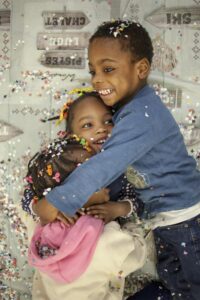 3 enfants se font un calin, ils et elles sont couvertes de confetti